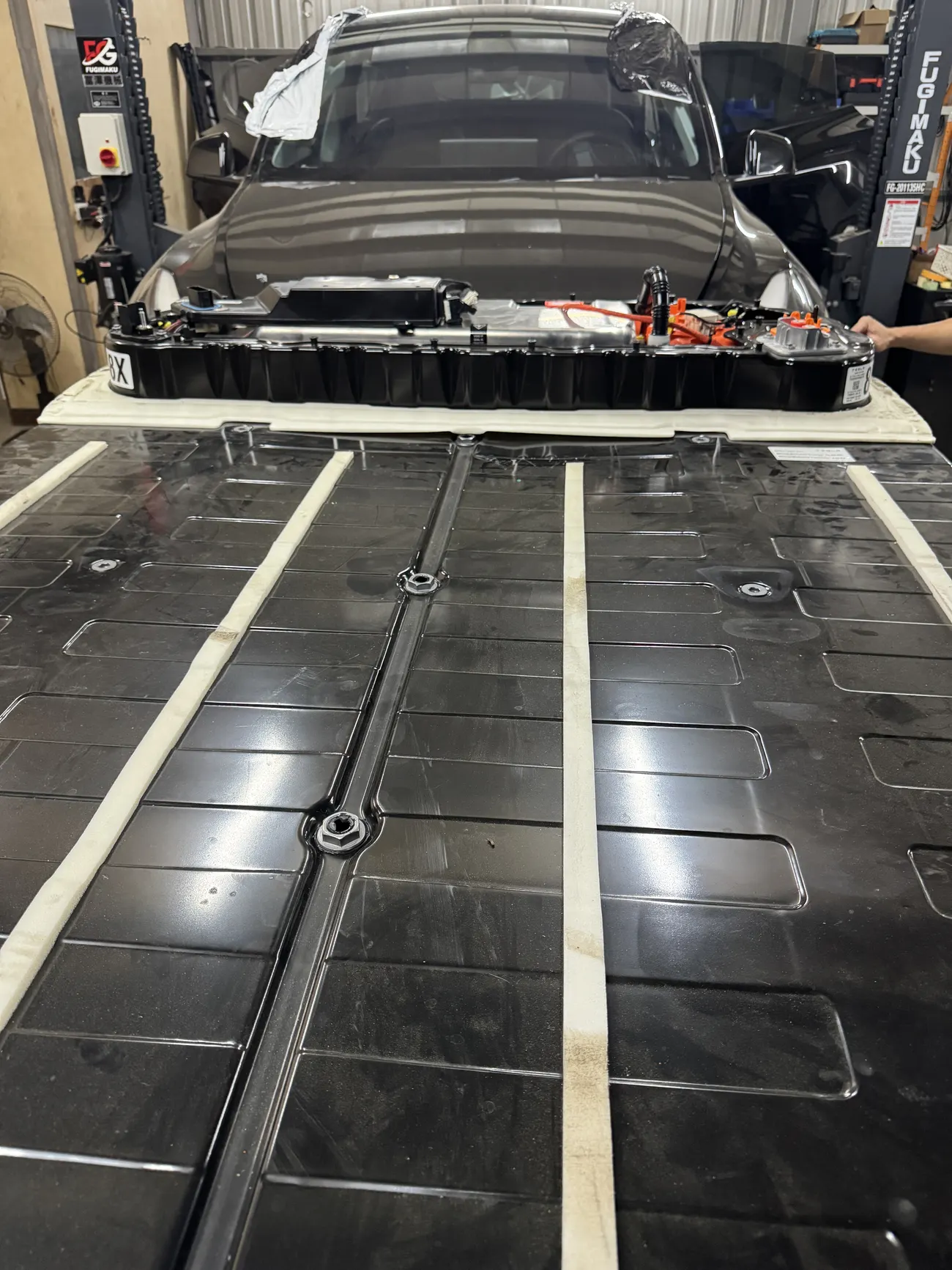 Tesla Model Y 事故車在升降機上，高壓電池包吊放在旁邊準備重新裝回車身
